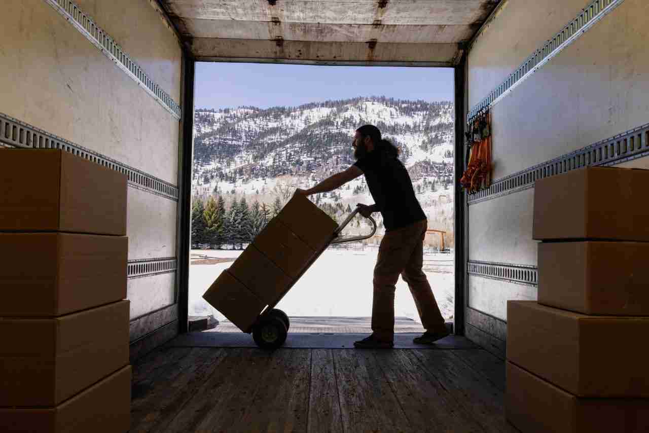 Mitarbeiter lädt Umzugskartons mit einer Sackkarre in den Transporter